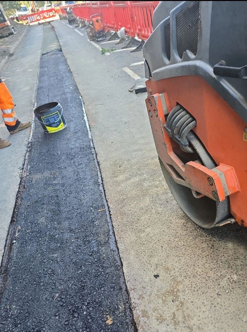 Roller finishing new surfacing beside a trench reinstatement