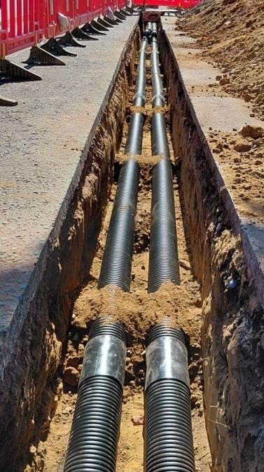 Twin power ducts laid in an open trench beside red safety barriers